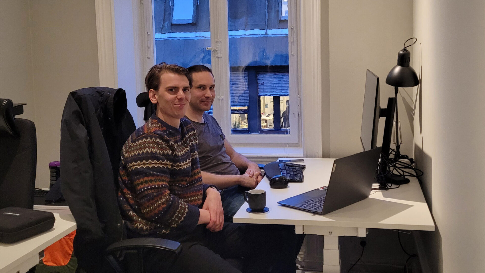 A sign that says Pugstorm and two men sitting by a desk.